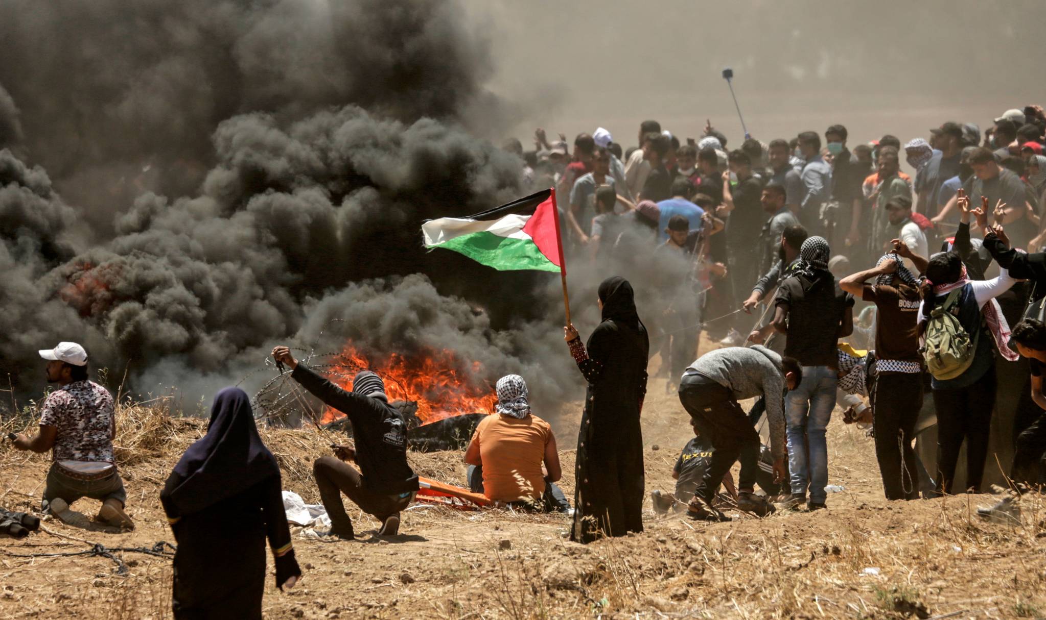 14일 가자지구에서 한 팔레스타인 여성이 국기를 들고 시위를 지켜보고 있다. [ AFP =연합뉴스]