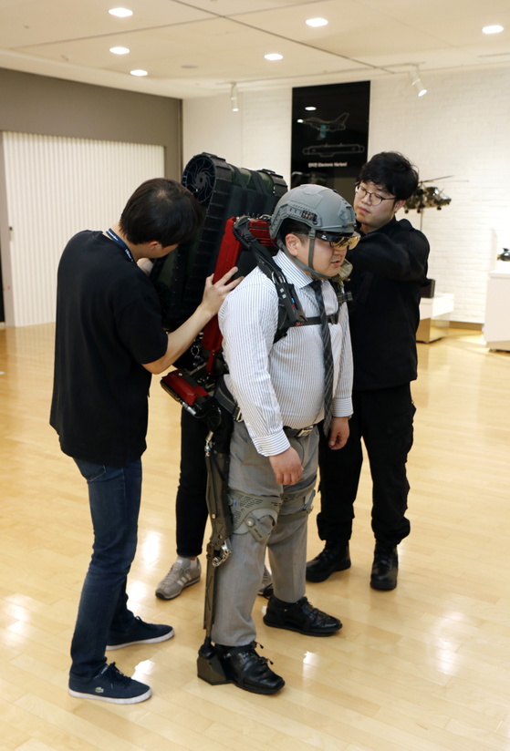 지난달 15일 LIG 넥스원 연구원이 LEXO를 착용한 취재 기자 어깨에 15㎏ 무인 로봇을 올리고 있다. [사진 LIG 넥스원]