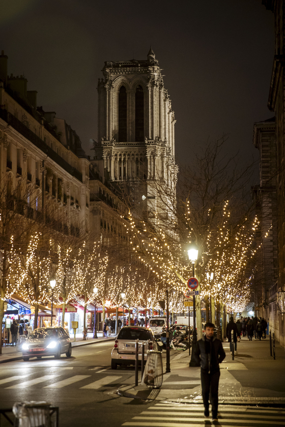 크리스마스를 이틀 앞둔 지난해 12월 23일 프랑스 파리의 화려한 거리 조명 뒤 불꺼진 노트르담 대성당의 보습이 보인다. 노트르담 성당은 화재로 인한 복구 작업으로 216년만에 처음으로 지난해 크리스마스 미사를 열지 못했다. [AP=연합뉴스]