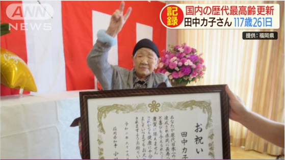 지난 19일 일본 최고령 다나카 카코 할머니가 후쿠오카현 지사로부터 축하장을 받은 뒤 손으로 브이자를 하고 있다. [TV아사히 캡쳐]