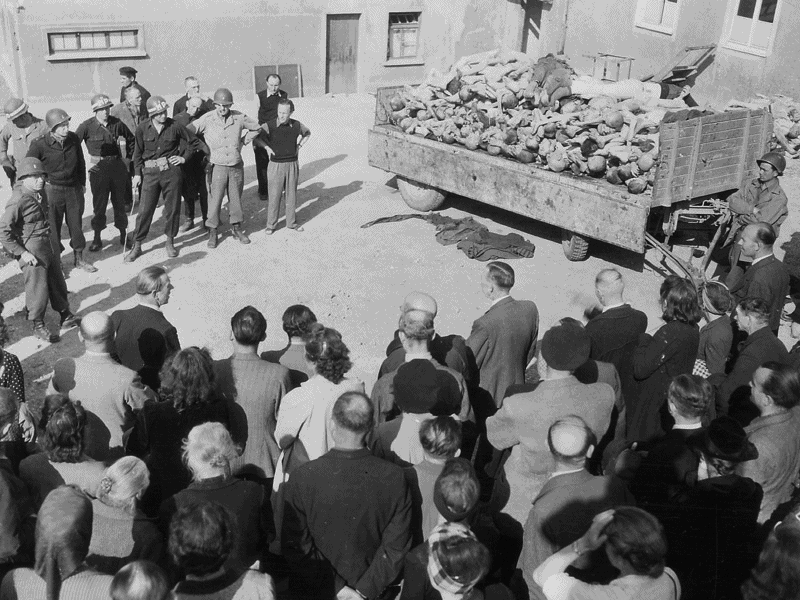 [1945年にドイツを占領した米軍に連れられ、強制収容所に入って惨状を見ているドイツ人ナチスのジャンホクサンを示すことは非ナチ化の開始である。写真=米国国立公文書館