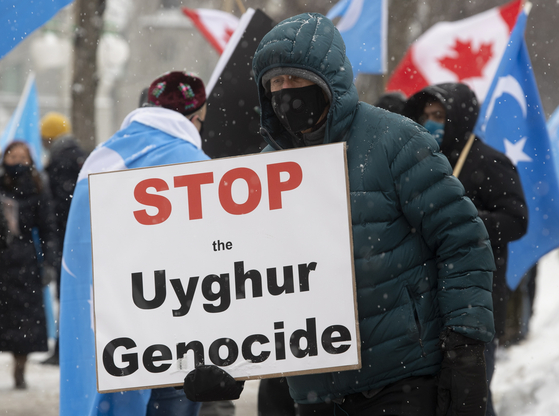 22일(현지시간) 캐나다 오타와에 위치한 의회 건물 앞에서 한 시위자가 "위구르족 학살을 멈추라"는 푯말을 들고 시위를 벌이고 있다. [AP=연합뉴스]