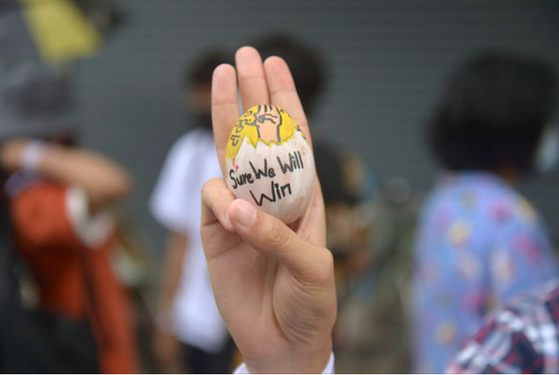 미얀마 양곤의 한 시위대가 '우리는 승리할 것'이라는 메시지가 새겨진 달걀을 들고 세 손가락 경례를 하고 있다.[AP=연합뉴스]